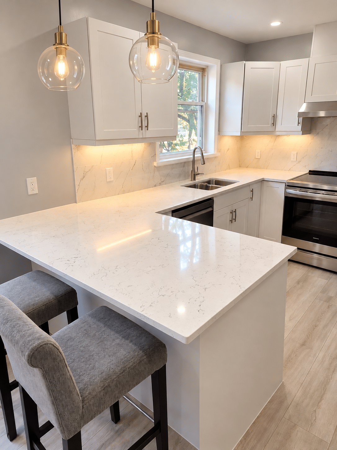 Modern kitchen renovation featuring white cabinetry, quartz-look countertops, breakfast peninsula, and pendant lighting