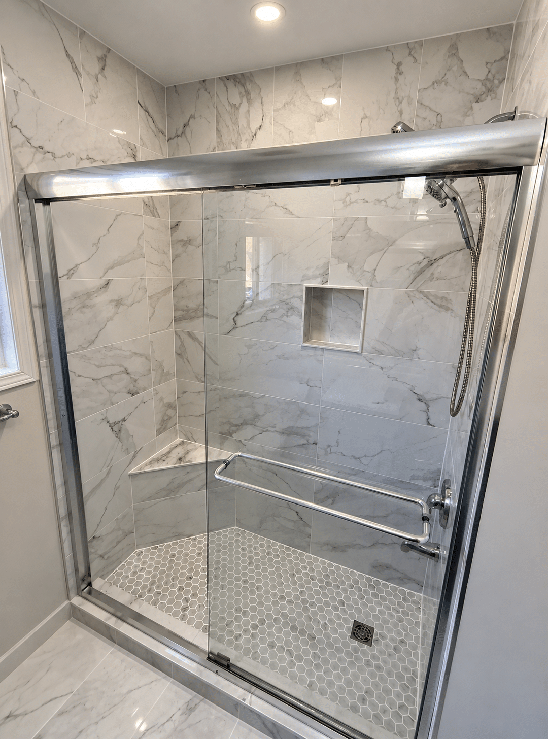 Tiled walk-in shower featuring marble-look wall tiles, hexagonal mosaic flooring, sliding glass doors, chrome shower fixtures, a recessed shower niche, and a corner bench.