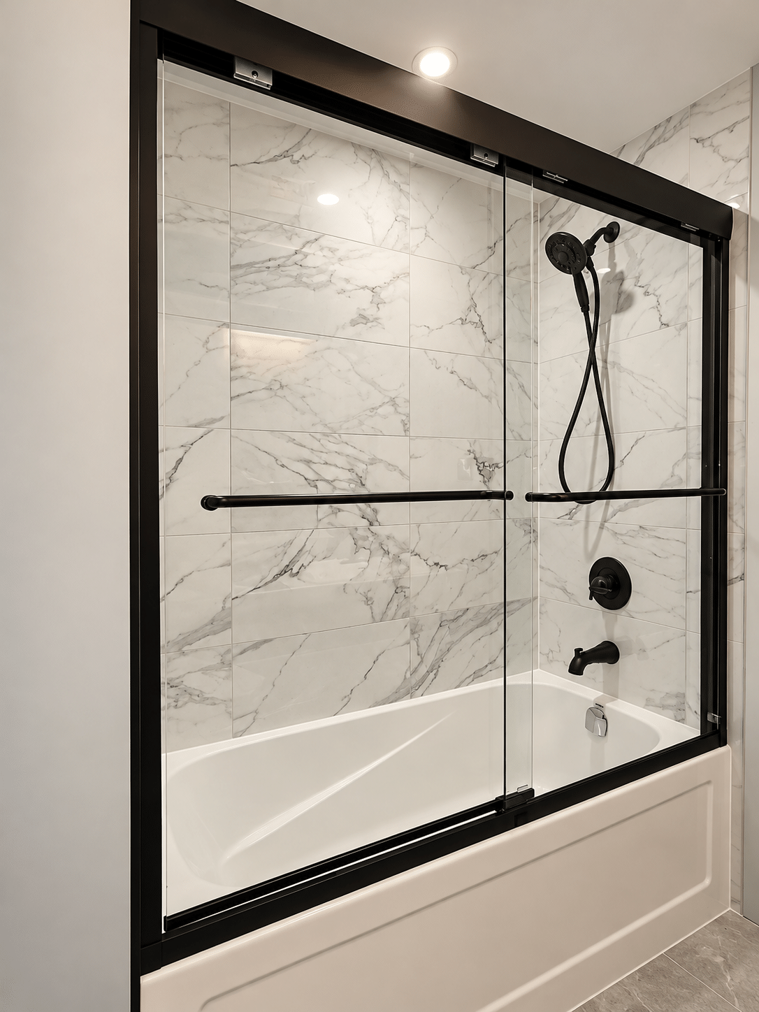 Modern bathroom renovation featuring a white bathtub, marble-look wall tiles, black-framed sliding glass shower doors, and matte black shower fixtures.