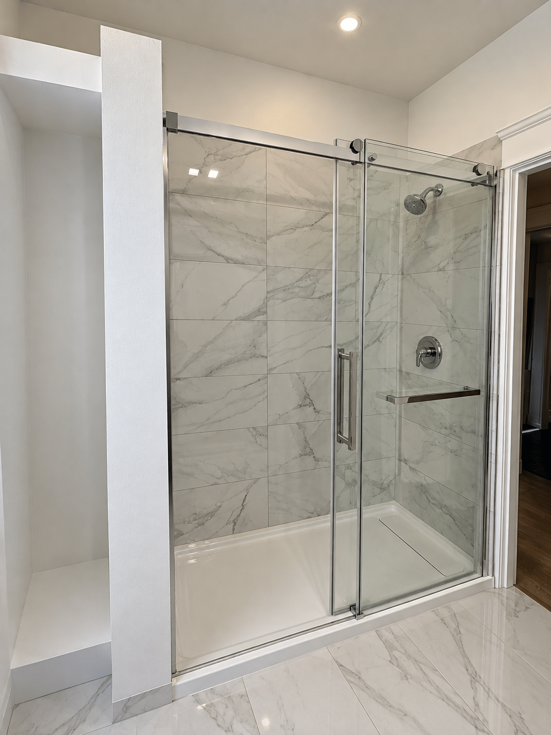 Walk-in shower renovation featuring marble-look porcelain tiles, a frameless sliding glass enclosure, chrome shower fixtures, and a white shower base.