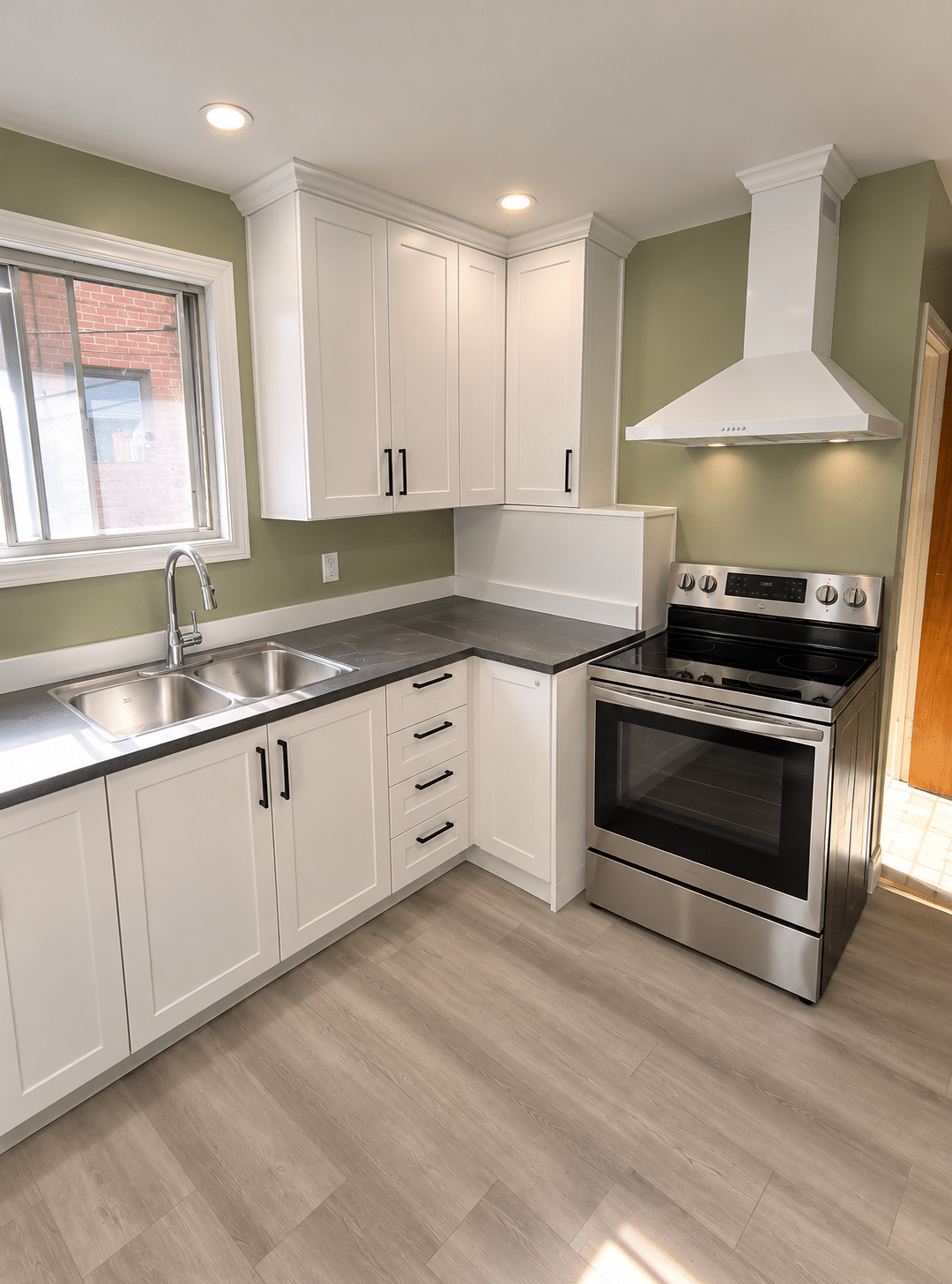 Kitchen renovation featuring white shaker cabinets, dark countertops, stainless steel appliances, and wood-look flooring